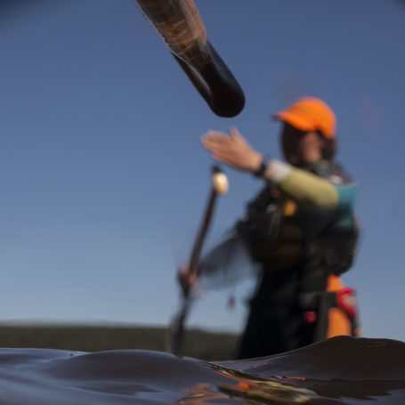 Paddler mit orangefarbener Mütze, hält einen Paddel vor einem ruhigen Gewässer.